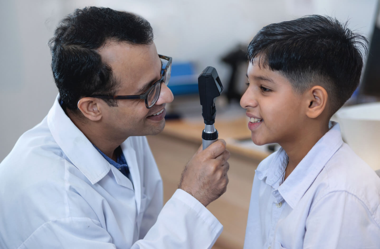 An optometrist conducts an eye exam on a child using an instrument called a direct ophthalmoscope.