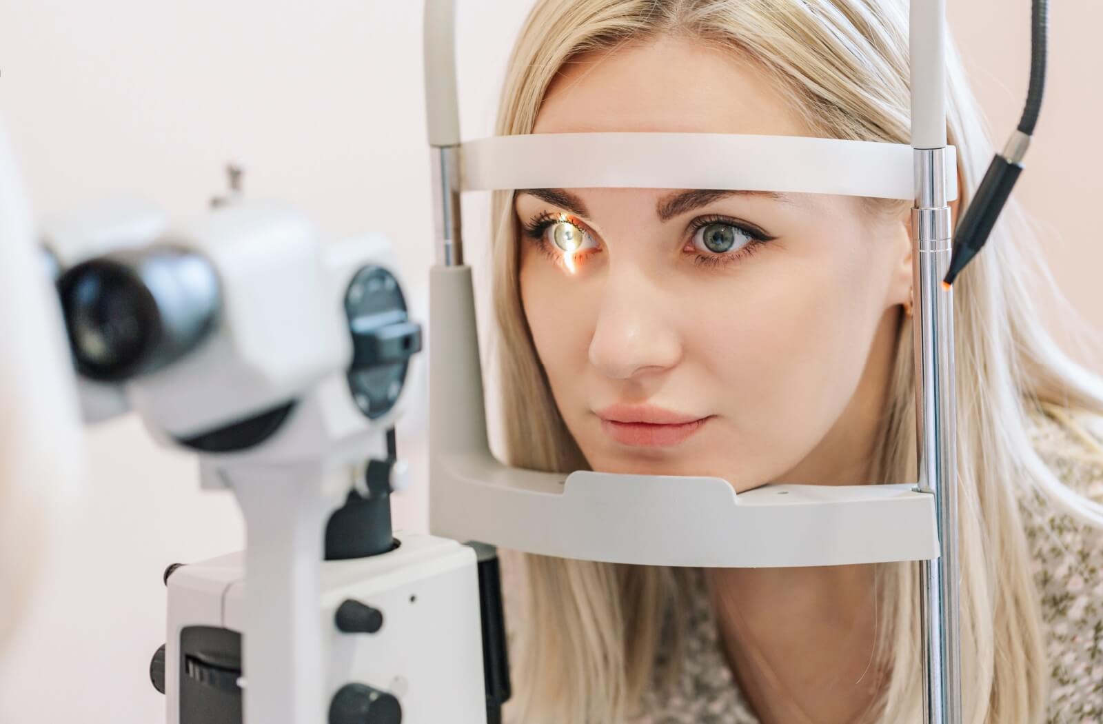 A smiling young woman undergoing a part of a comprehensive eye examination involving a biomicroscope, or slit lamp.