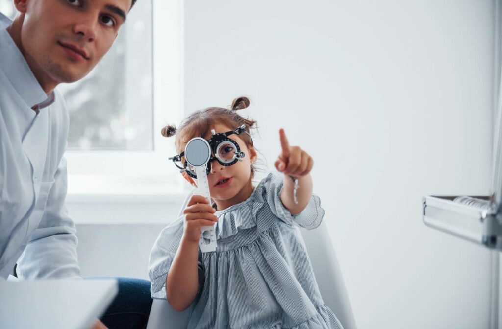 A young girl holds up an eye test during an annual eye exam for myopia. She points to the wall with her optometrist beside her