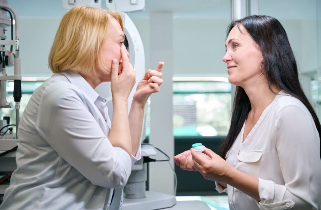 In a brightly lit office, an optometrist holds a contact lenses case while teaching a patient how to insert their contact lenses.